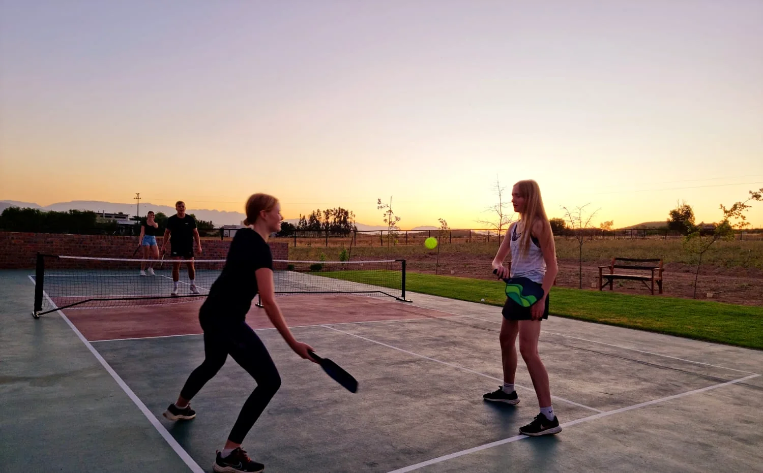 Guests playing pickleball on the Klawerjas court at sunset
